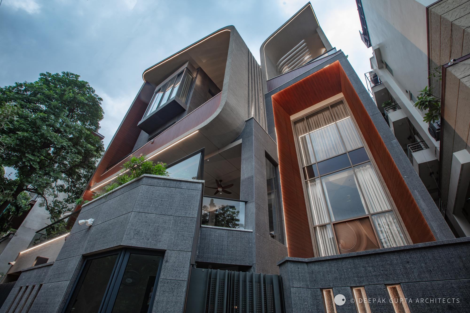 GK Residence: curved upper floors wrapped in bronze-red fins above a dark stone base